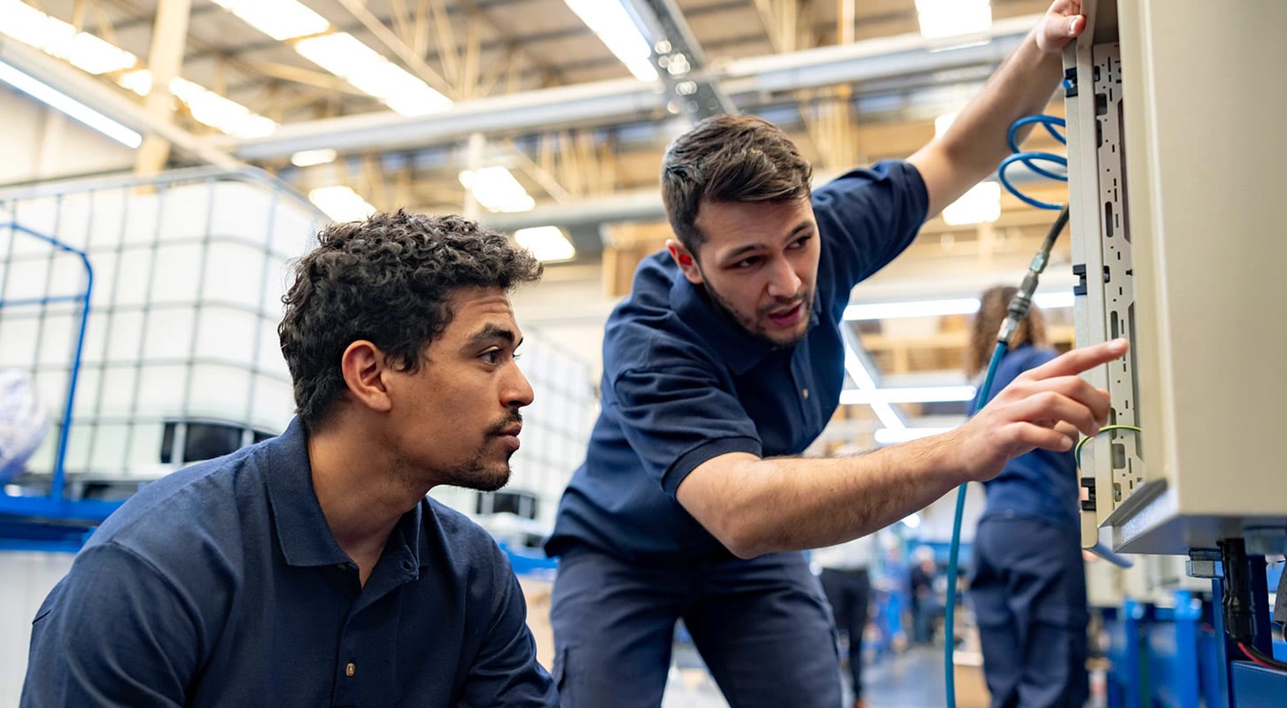 Two workers collaborating on a machine in an industrial environment.